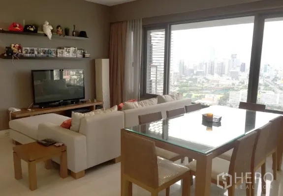 公寓 出租或出售在Sathon, Bangkok - 客厅电视区与玻璃餐桌，整面落地窗对望天际线与大片绿地景观。