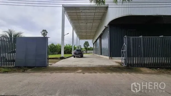Warehouse for rent in Mueang Nonthaburi, Nonthaburi - Gated driveway leading to the warehouse under a large canopy with parking and turning space.