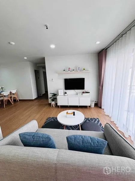 คอนโด ให้เช่าในWatthana, Bangkok - มุมมองพื้นที่นั่งเล่นโล่งไปยังตู้ทีวีและระเบียง พื้นไม้และพรมลายเรขาคณิต
