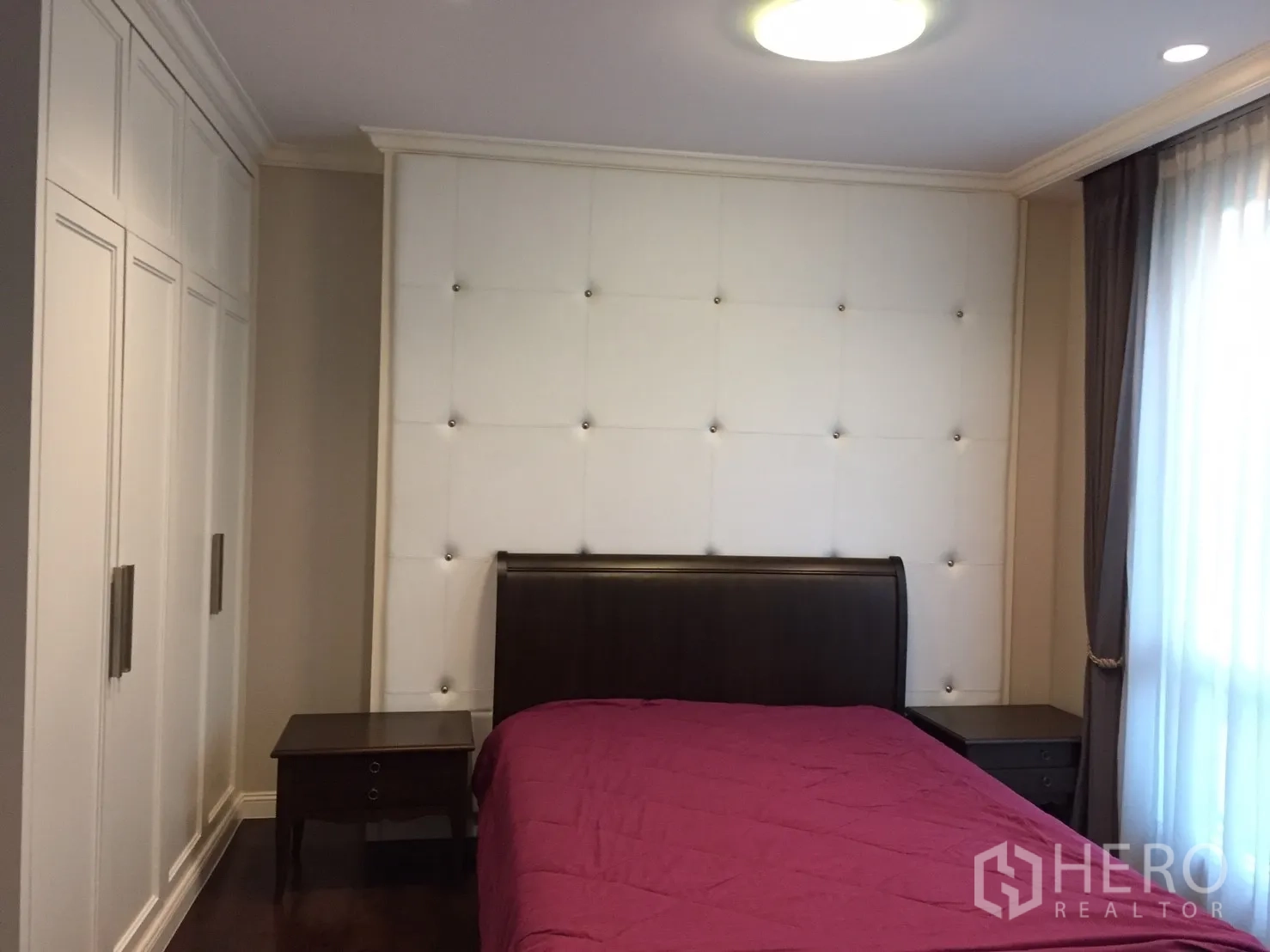 คอนโด ขายในHuai Khwang, Bangkok - ห้องนอนหลักผนังหัวเตียงบุกุ้ม บุ๋ม พร้อมเตียงไม้สีเข้มและตู้เสื้อผ้าบิวท์อิน