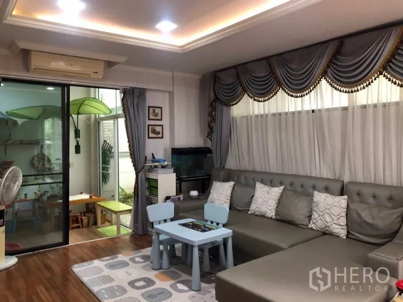 独立式住宅 出售在Lam Luk Ka, Pathum Thani - 家庭起居室，大型转角沙发，儿童游戏区，推拉玻璃门通向日光房。