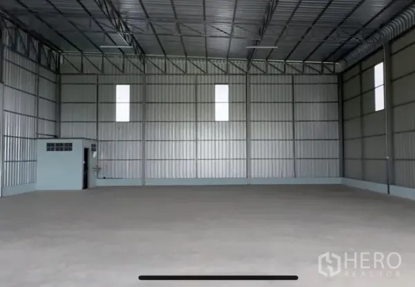 Warehouse for rent in Lam Luk Ka, Pathum Thani - Open warehouse bay showing tall ceiling, metal wall panels and a built-in restroom in the corner.
