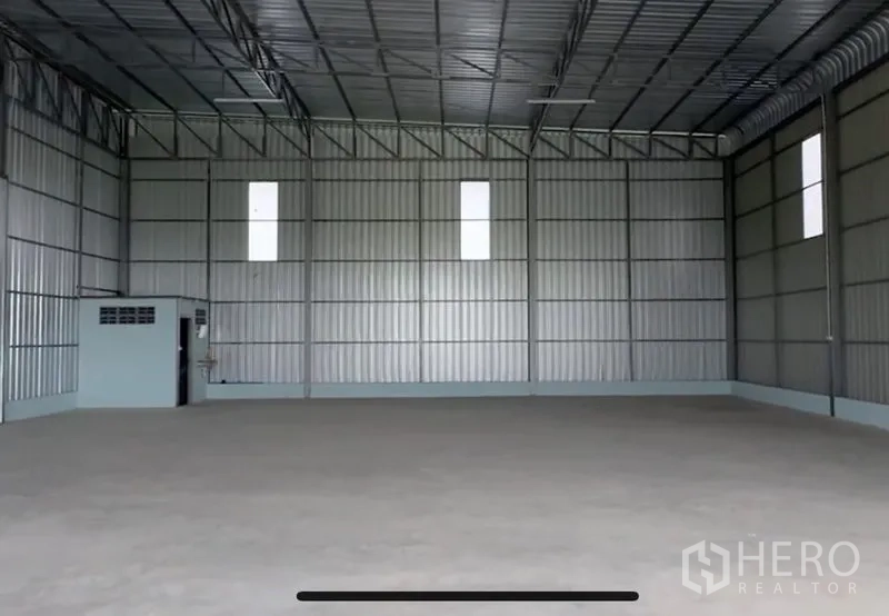 Warehouse for rent in Lam Luk Ka, Pathum Thani - Open warehouse bay showing tall ceiling, metal wall panels and a built-in restroom in the corner.