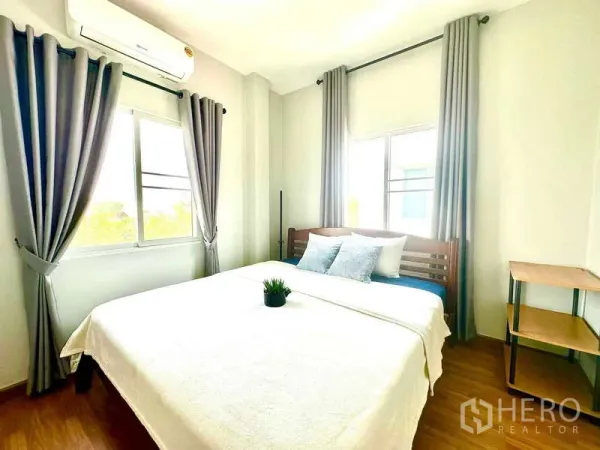 Detached House for rent in Lat Krabang, Bangkok - Sunlit bedroom with double bed, air conditioner, gray curtains and wood flooring.