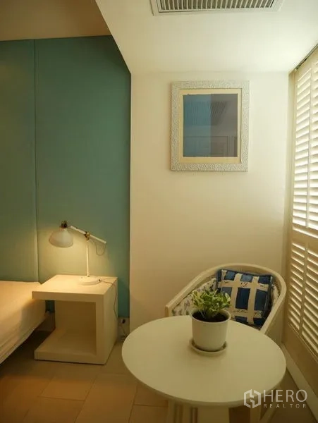 Condominium for rent in Khlong Toei, Bangkok - Compact reading nook with round table, chair and a potted plant.