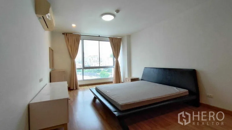 Condominium for rent in Khlong Toei, Bangkok - Spacious second bedroom with platform bed, wide window, city views and neutral curtains.
