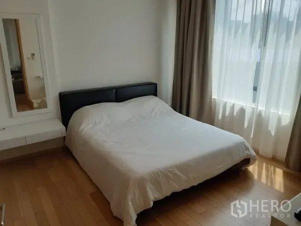 Condominium for rent in Khlong Toei, Bangkok - Cozy bedroom with queen bed, wood floors and a large window with sheer and blackout curtains.