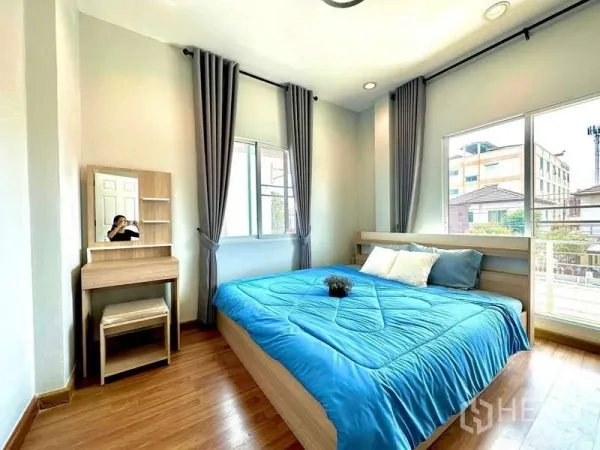 Detached House for rent in Lat Krabang, Bangkok - Bright bedroom with large windows, gray curtains, wooden floor, blue bedding and a vanity table.