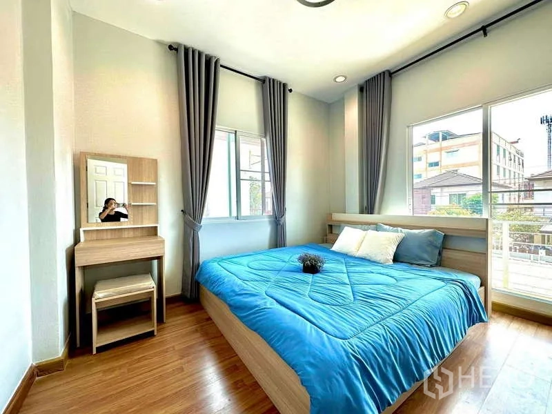 Detached House for rent in Lat Krabang, Bangkok - Bright bedroom with large windows, gray curtains, wooden floor, blue bedding and a vanity table.