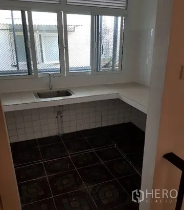 Shophouse for rent in Watthana, Bangkok - Simple kitchen with single sink, tiled countertop and screened windows.