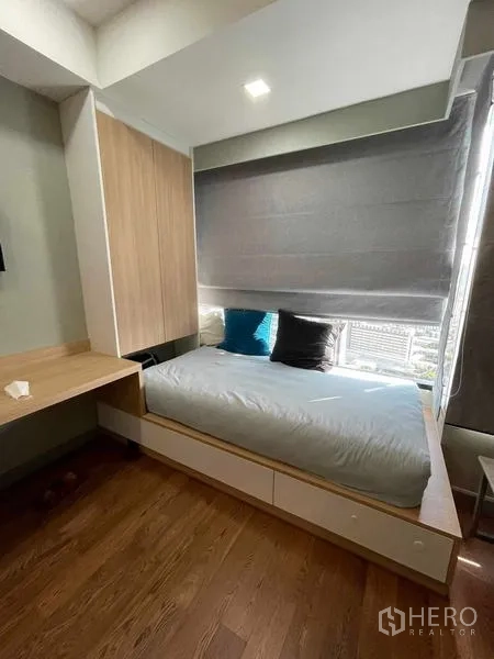 Condominium for rent or sale in Bang Rak, Bangkok - Cozy bedroom with a platform bed with drawers, window shades, and a city view.