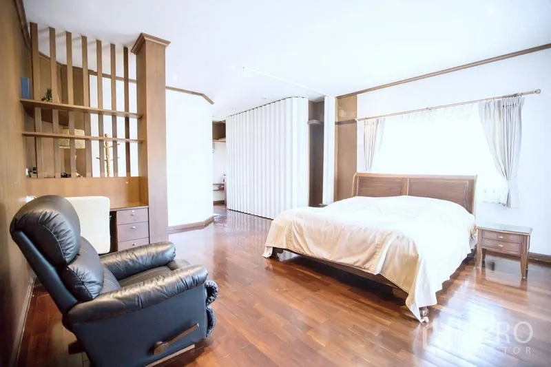 Detached House for sale in Lat Krabang, Bangkok - Spacious master bedroom with wooden flooring, large bed, recliner and divider shelves.