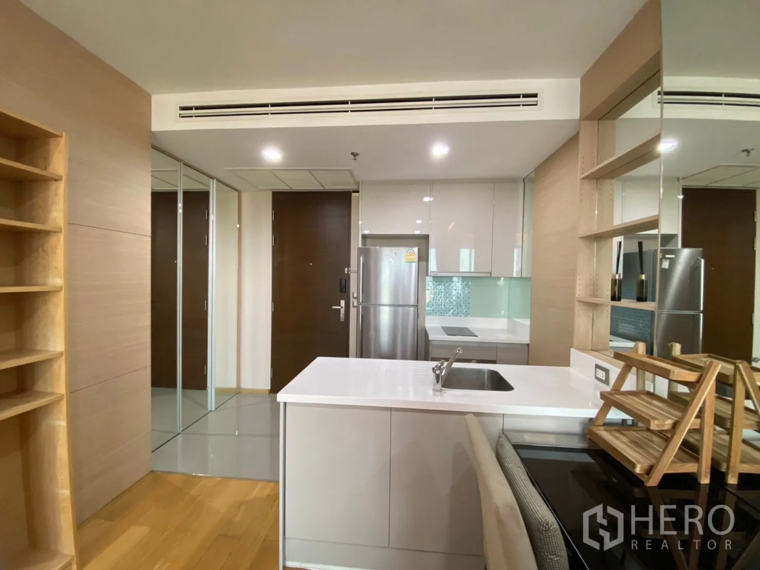 公寓 出租在Ratchathewi, Bangkok - 现代小厨房，白色中岛、内置搁架、镜面柜门与不锈钢冰箱，曼谷公寓室内。