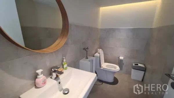 Detached House for rent in Watthana, Bangkok - Guest bathroom with large round mirror, vanity and toilet.