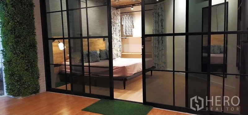Condominium for sale in Watthana, Bangkok - Bedroom behind black-framed glass partition with warm lighting and wood accents in a modern condo.