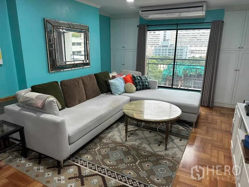 Condominium for sale in Bangkok - Bright living room with teal walls, L‑shaped sofa, marble coffee table and city-view window.