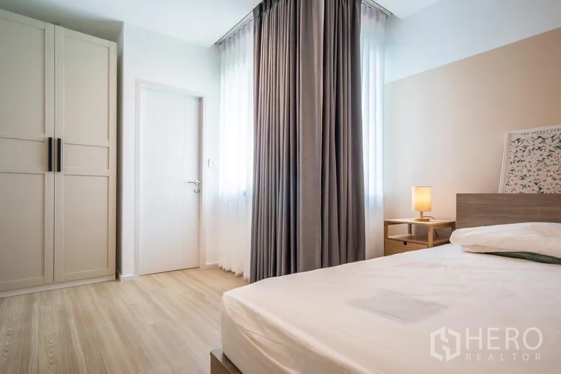 Townhouse for rent or sale in Suan Luang, Bangkok - Bedroom with double bed, freestanding wardrobe, bedside lamp, and window light.
