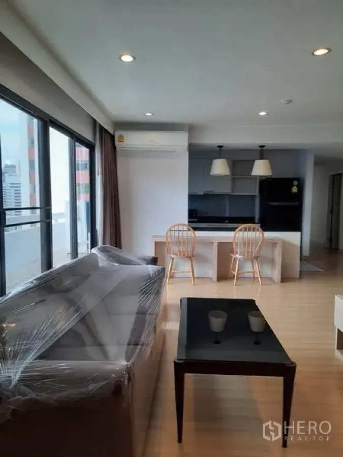 Condominium for rent in Watthana, Bangkok - Bright open-plan living and dining area with large windows, sofa, and a kitchen island in a Sukhumvit condo near Asok.