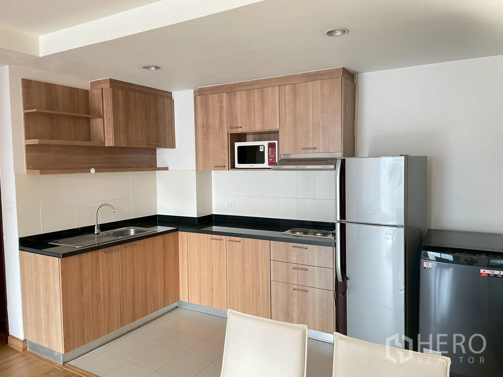 อพาร์ทเมนท์ for rent in Khlong Toei, Bangkok - ครัวรูปตัวแอล ผนังกระเบื้อง ท็อปสีดำ และตู้เย็นขนาดใหญ่