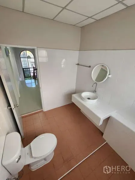 联排别墅 出租在Wang Thonglang, Bangkok - 明亮的卫生间，白色瓷砖墙、圆镜、洗手台与坐便器。