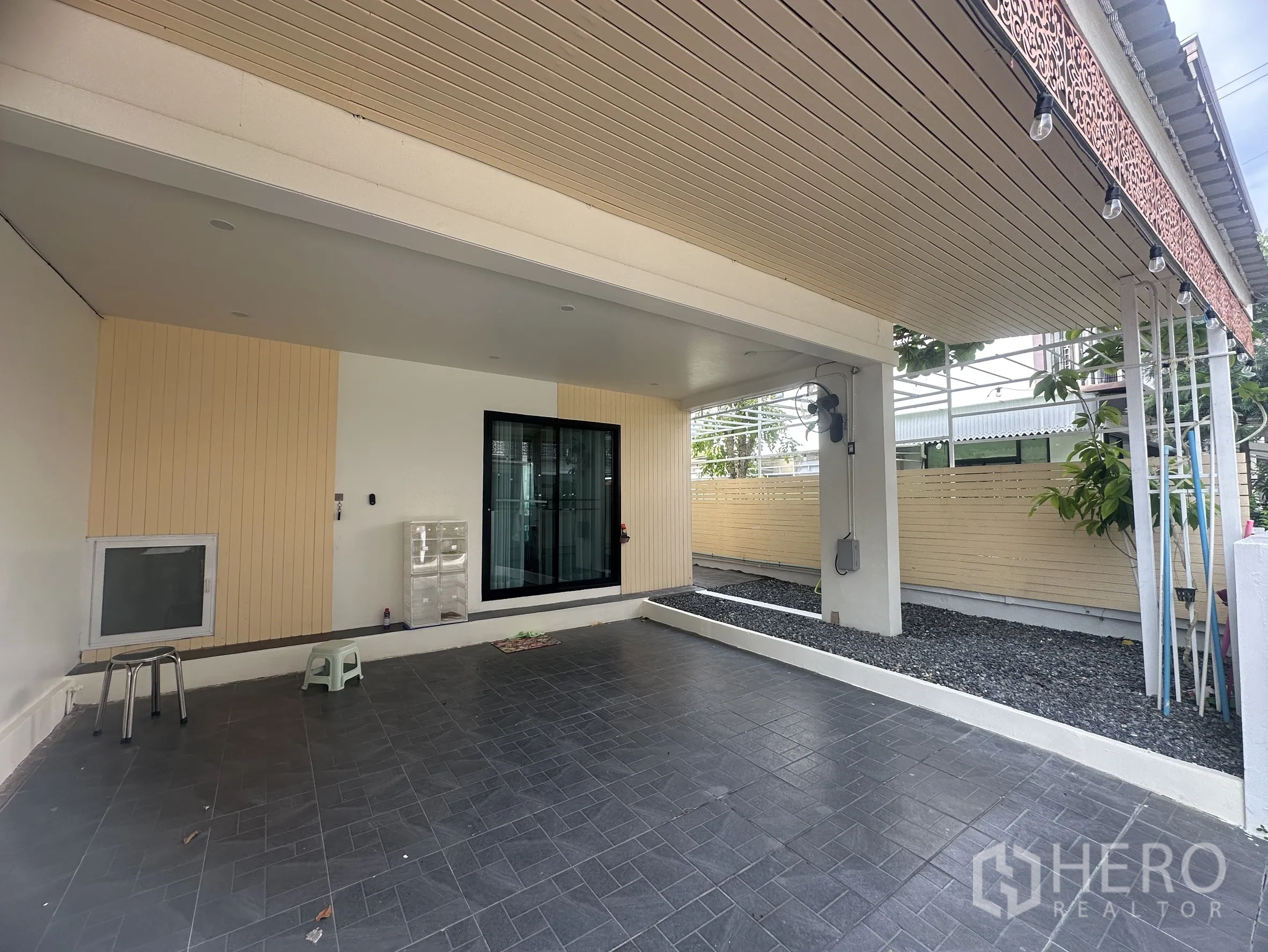 Townhouse for sale in Lam Luk Ka, Pathum Thani - Covered carport with tiled floor and sliding glass door to the living area.