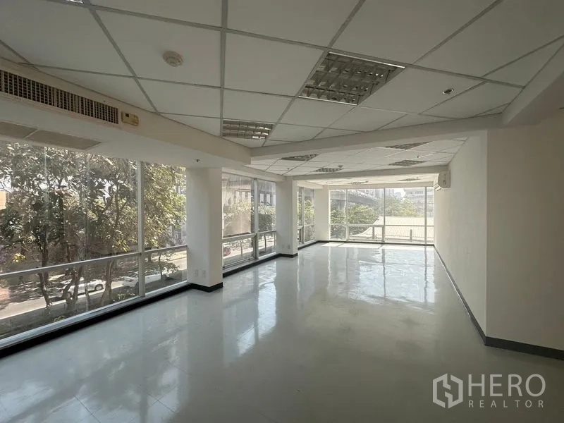 办公空间 出租在Phaya Thai, Bangkok - 明亮的转角办公区，环绕落地窗与吊顶灯，可见绿树景观。