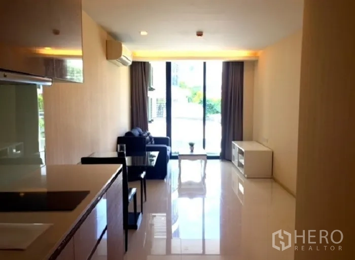 公寓 出租或出售在Pathum Wan, Bangkok - 明亮客厅设沙发与餐桌，推拉门通阳台，旁为小厨房。