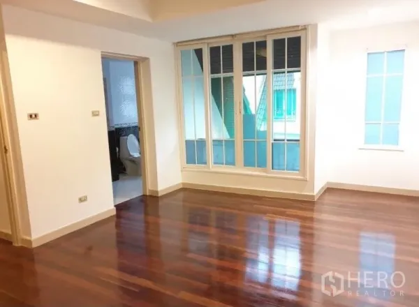 Townhouse for rent or sale in Chatuchak, Bangkok - Spacious room with polished wooden floors, large window panels and an en-suite bathroom doorway.