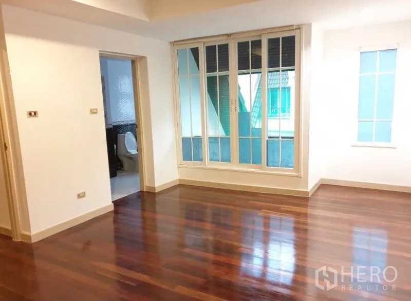 Townhouse for rent or sale in Chatuchak, Bangkok - Spacious room with polished wooden floors, large window panels and an en-suite bathroom doorway.