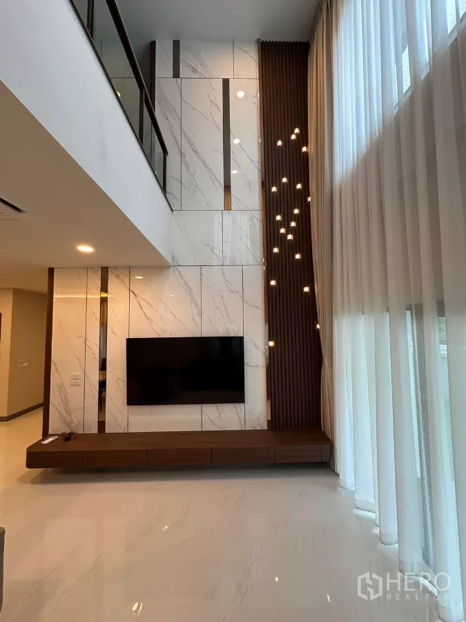 独立式住宅 出租在Bang Phli, Samut Prakan - 挑高客厅，大理石特色墙、壁挂电视、纱帘与吊灯。