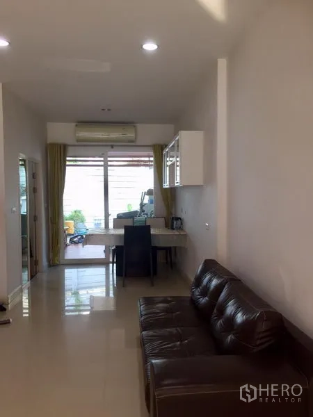 联排别墅 出租或出售在Wang Thonglang, Bangkok - 采光良好的客餐厅一体空间，皮沙发、亮面地砖、空调与通往小露台的推拉玻璃门。