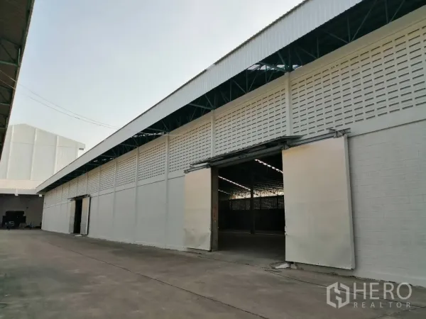 Warehouse for rent in Mueang Pathum Thani, Pathum Thani - Long warehouse facade with open sliding doors and a covered loading lane inside the compound.