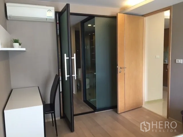 公寓 出租或出售在Pathum Wan, Bangkok - 卧室一角设有书桌与空调，玻璃门通往浴室。