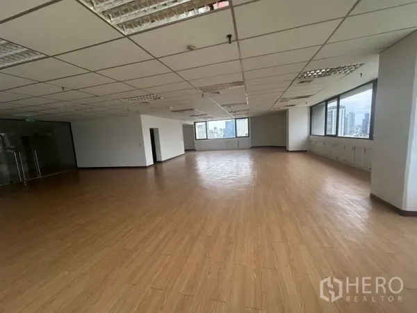Office Space for rent in Bang Rak, Bangkok - Spacious empty office with wood flooring, grid ceiling lights and glass entry, lined with windows overlooking skyscrapers