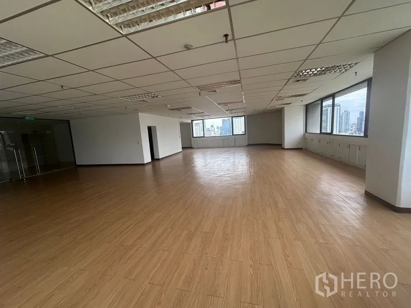 Office Space for rent in Bang Rak, Bangkok - Spacious empty office with wood flooring, grid ceiling lights and glass entry, lined with windows overlooking skyscrapers