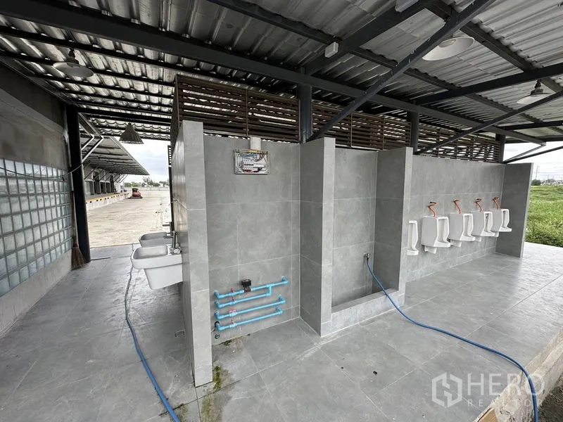 Factory for rent in Bang Sao Thong, Samut Prakan - Outdoor tiled washroom area with urinals and sinks beneath a metal roof.