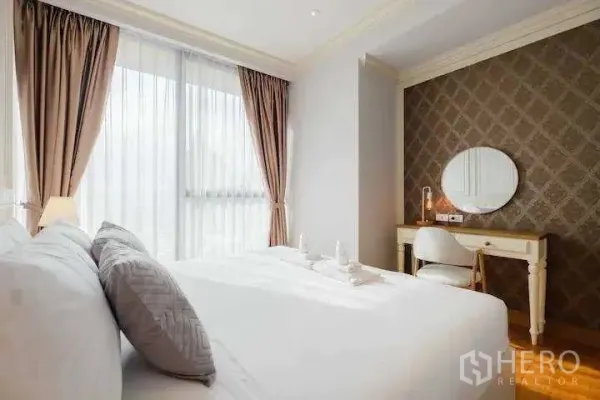 Condominium for rent in Khlong Toei, Bangkok - Cozy bedroom angle showing patterned accent wall, dressing table with round mirror, and large window.