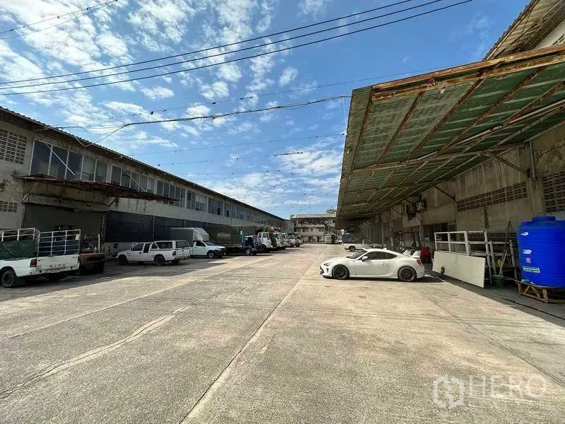 Factory for rent in Sai Noi, Nonthaburi - Another angle of the hard-stand yard with parking and a covered loading area along the building frontage.