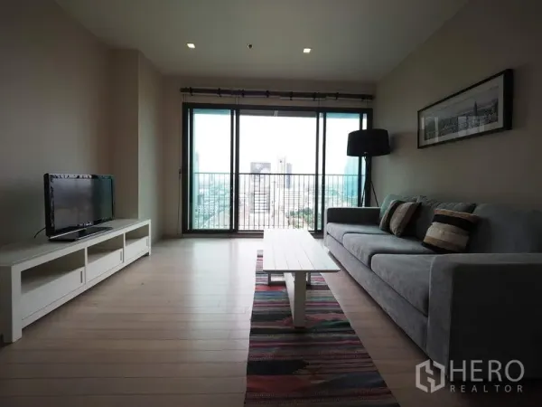 คอนโด ให้เช่าในWatthana, Bangkok - ห้องนั่งเล่นมีโซฟาสีเทา ชั้นวางทีวี และประตูกระจกบานเลื่อนมองเห็นวิวเมือง