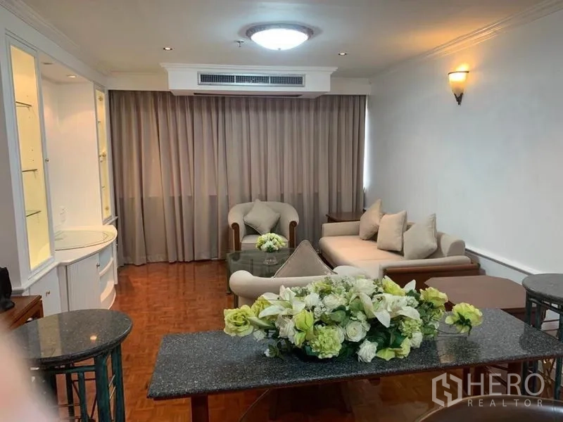 Condominium for sale in Watthana, Bangkok - Cozy living room with sofa set, armchairs, coffee table, and soft drapes across a wide window.