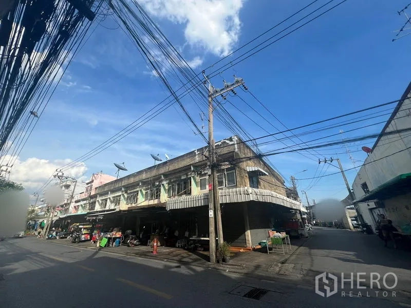 ที่ดิน ให้เช่าหรือขายในPhra Khanong, Bangkok - แถวย่านอาคารพาณิชย์สองชั้นตรงสี่แยกถนน พร้อมเสาไฟและสายสื่อสาร ท้องฟ้าสีคราม.