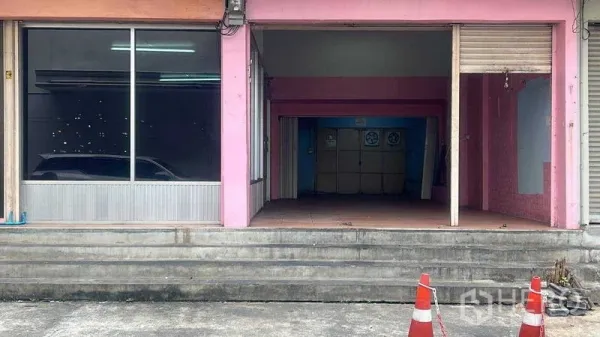零售空间 出租在Bang Na, Bangkok - 临街粉色门面，宽幅展示橱窗与半开启卷闸门，门前有台阶。