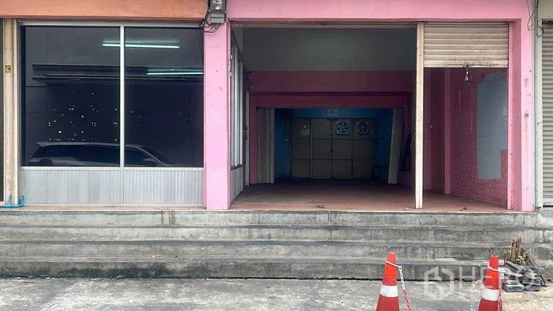 零售空间 出租在Bang Na, Bangkok - 临街粉色门面，宽幅展示橱窗与半开启卷闸门，门前有台阶。