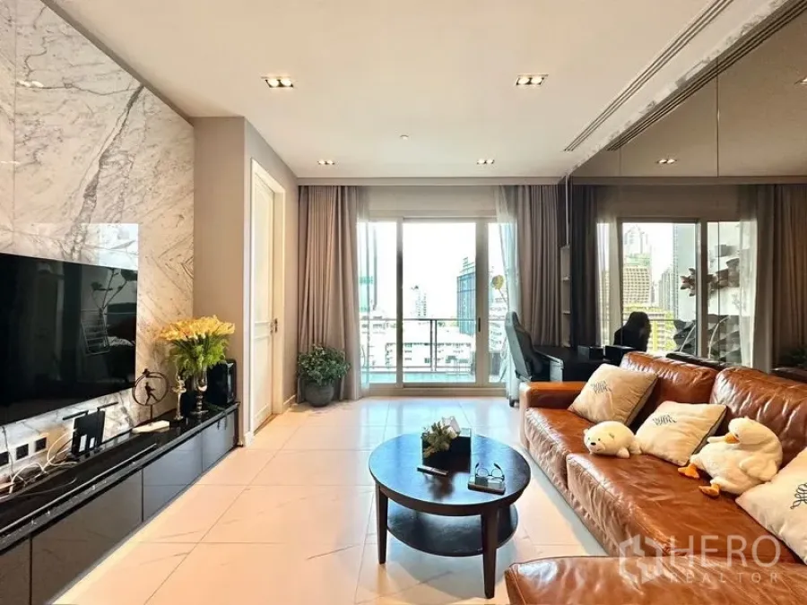 Condominium for rent in Pathum Wan, Bangkok - Bright living room with marble feature wall, leather sofa, TV console and balcony city view.