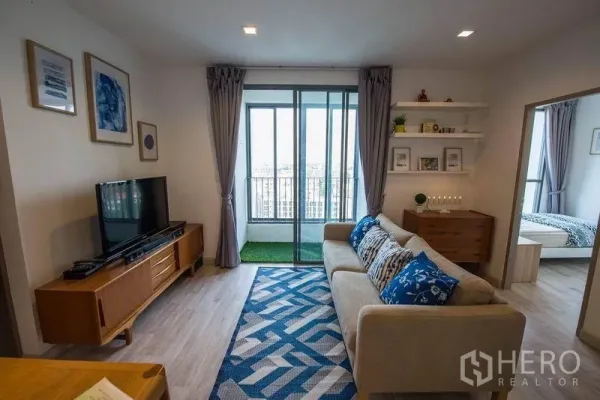 Condominium for rent in Phra Khanong, Bangkok - Lounge with wall shelves, sofa and access to bedrooms and balcony.