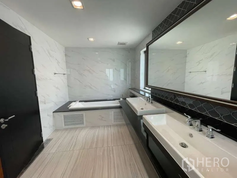 Detached House for rent or sale in Lat Krabang, Bangkok - Master bathroom featuring double sinks, a wide mirror and a bathtub beside a bright window.