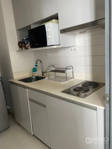 Condominium for sale in Phra Khanong, Bangkok - Compact white kitchenette with sink, cooktop, range hood and microwave