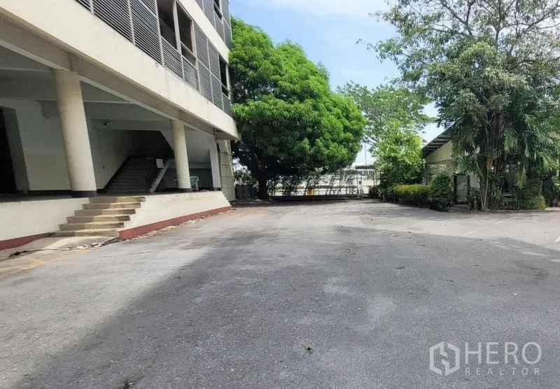 Factory for rent in Mueang Samut Prakan, Samut Prakan - Spacious driveway and on-site parking beside the building with mature trees