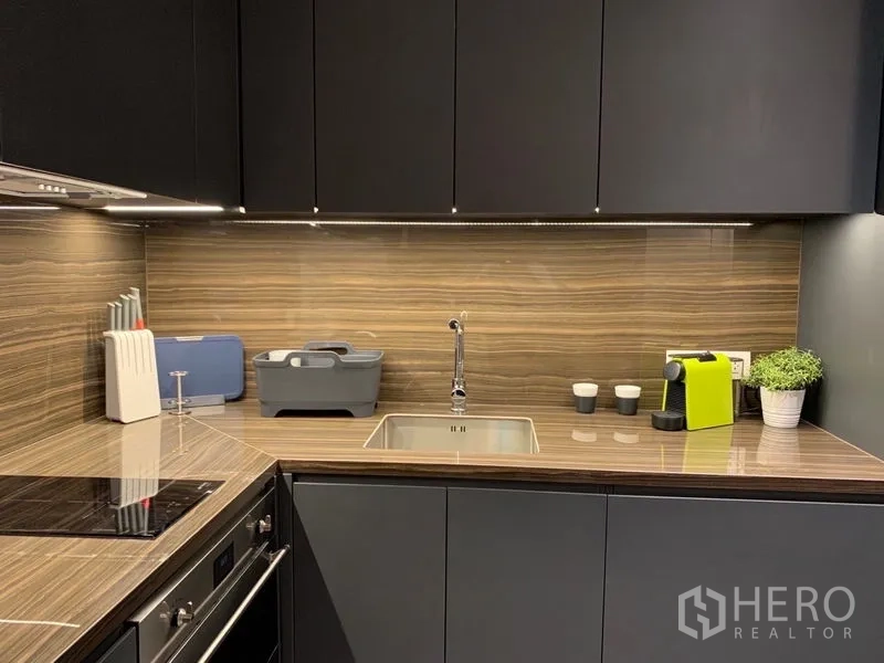 Condominium for rent in Bang Rak, Bangkok - Kitchen countertop with wood-grain backsplash, sink and espresso machine.