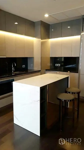 Condominium for rent in Watthana, Bangkok - Sleek kitchen featuring a marble island, bar stools and two-tone cabinetry with under-cabinet lighting.